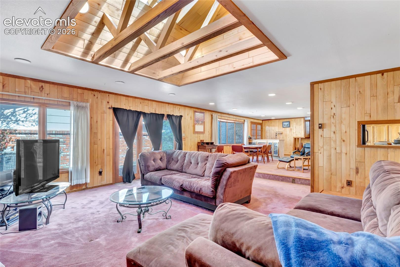 Wood-paneled walls and ceiling accents, recessed lighting, and large windows