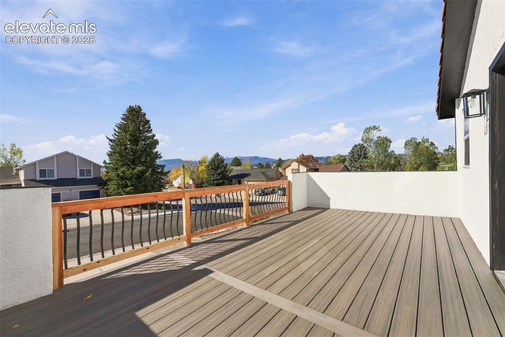 Elevated deck featuring composite wood-finish decking, a wooden perimeter rail with metal balusters, and stucco wall partitions