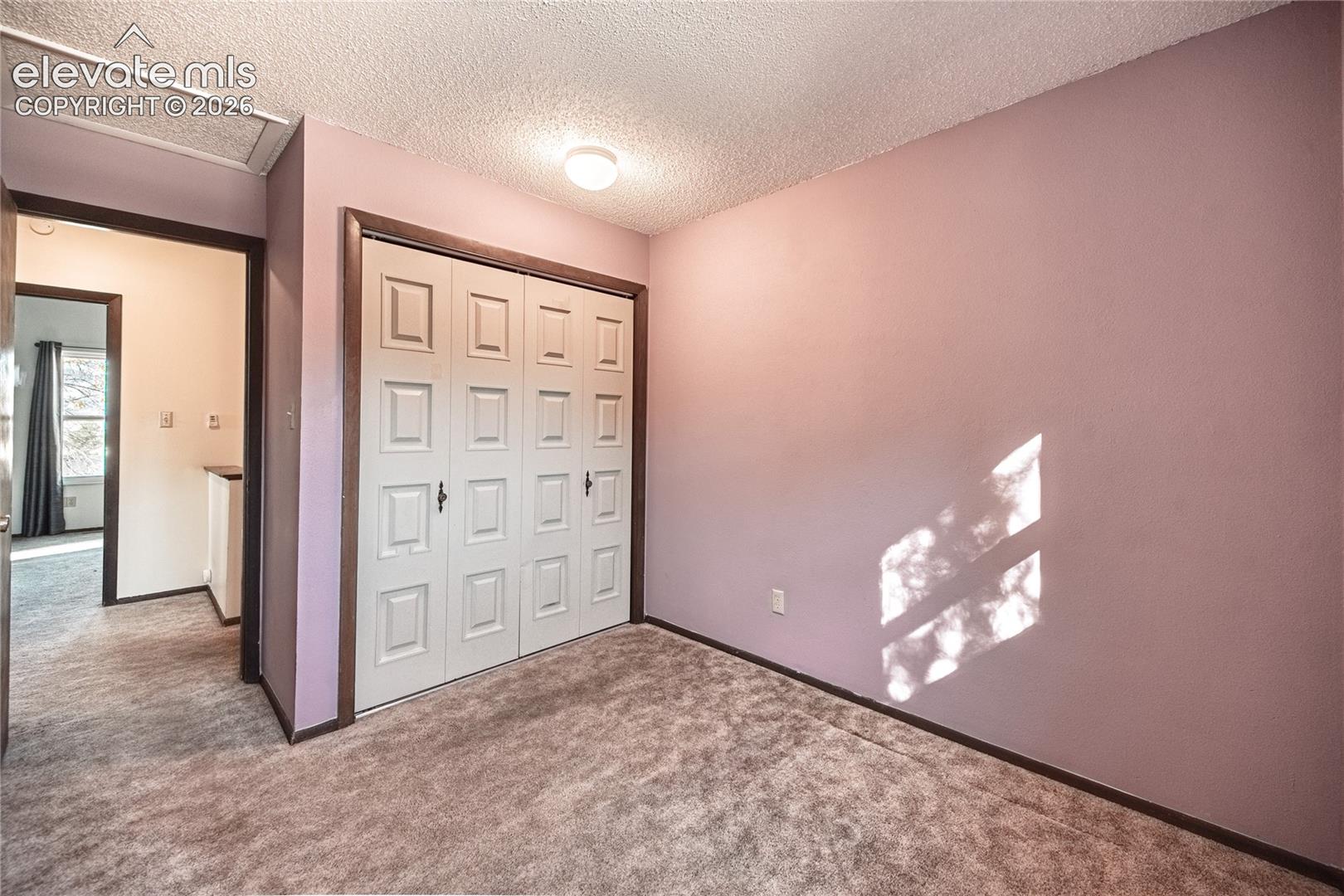 Bedroom featuring wall-to-wall carpeting, bi-fold closet doors with raised panels, and ceiling-mounted lighting