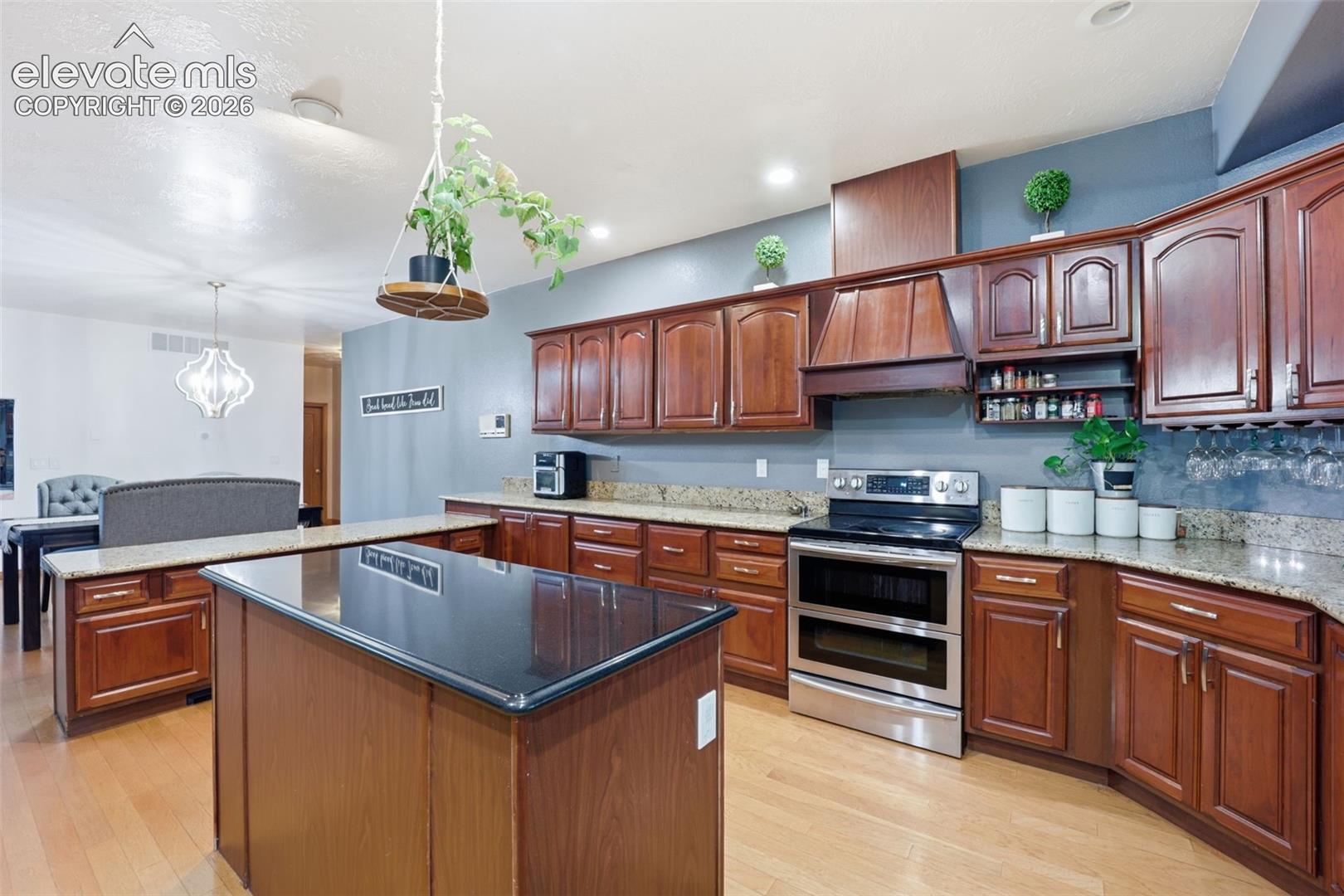 Kitchen featuring wood cabinetry, granite countertops, a central island with a dark countertop, stainless steel appliances, and wood-finish flooring