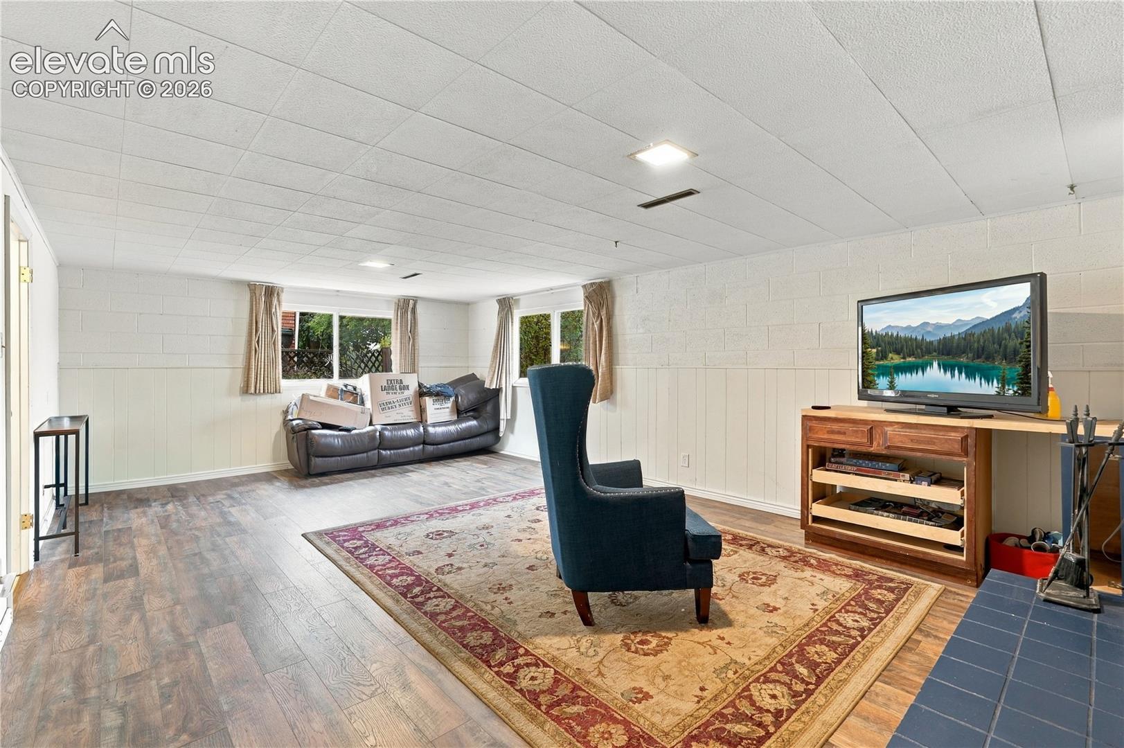 Interior space featuring wood-finish flooring, painted masonry walls, beadboard wainscoting, a drop ceiling with recessed lighting, and multiple windows