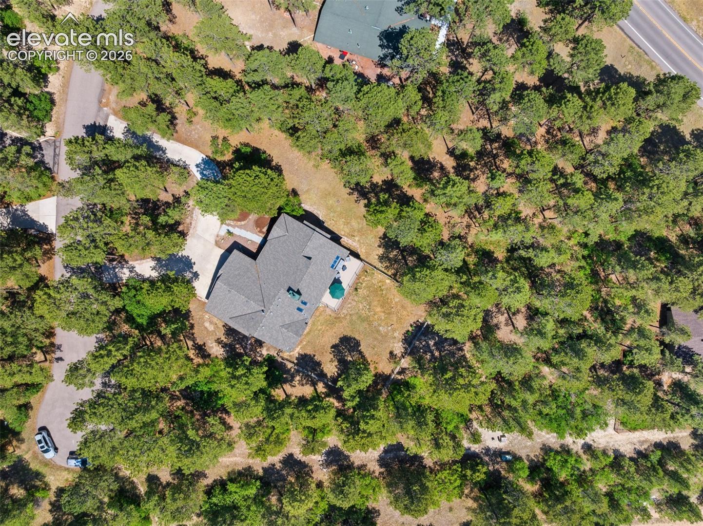 Single-story residence set on a treed lot, featuring a grey shingle roof and a concrete driveway
