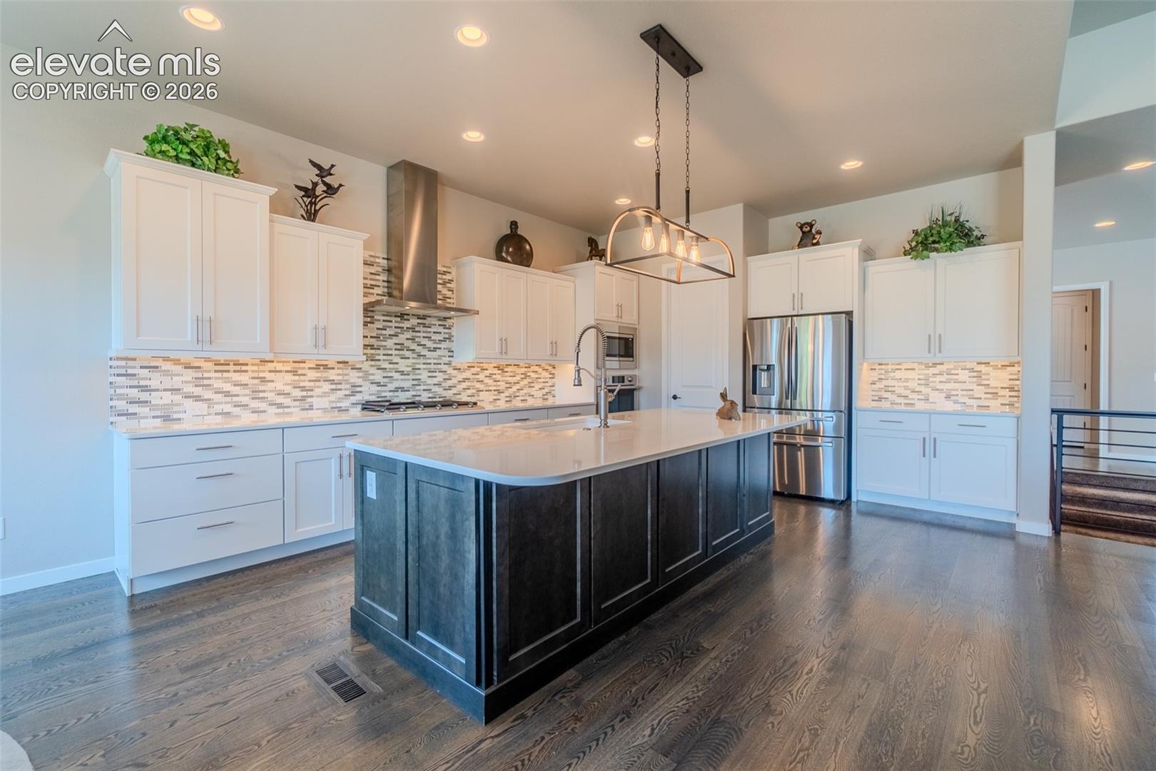 Spacious kitchen featuring an oversized island with a light-toned countertop, stainless steel appliances, white cabinetry, a tiled backsplash, and wood-finish flooring