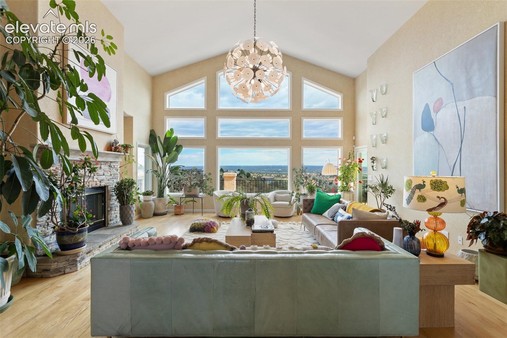 Vaulted living space featuring a stacked stone fireplace, wood-finish flooring, and a multi-pane picture window providing expansive exterior scenery