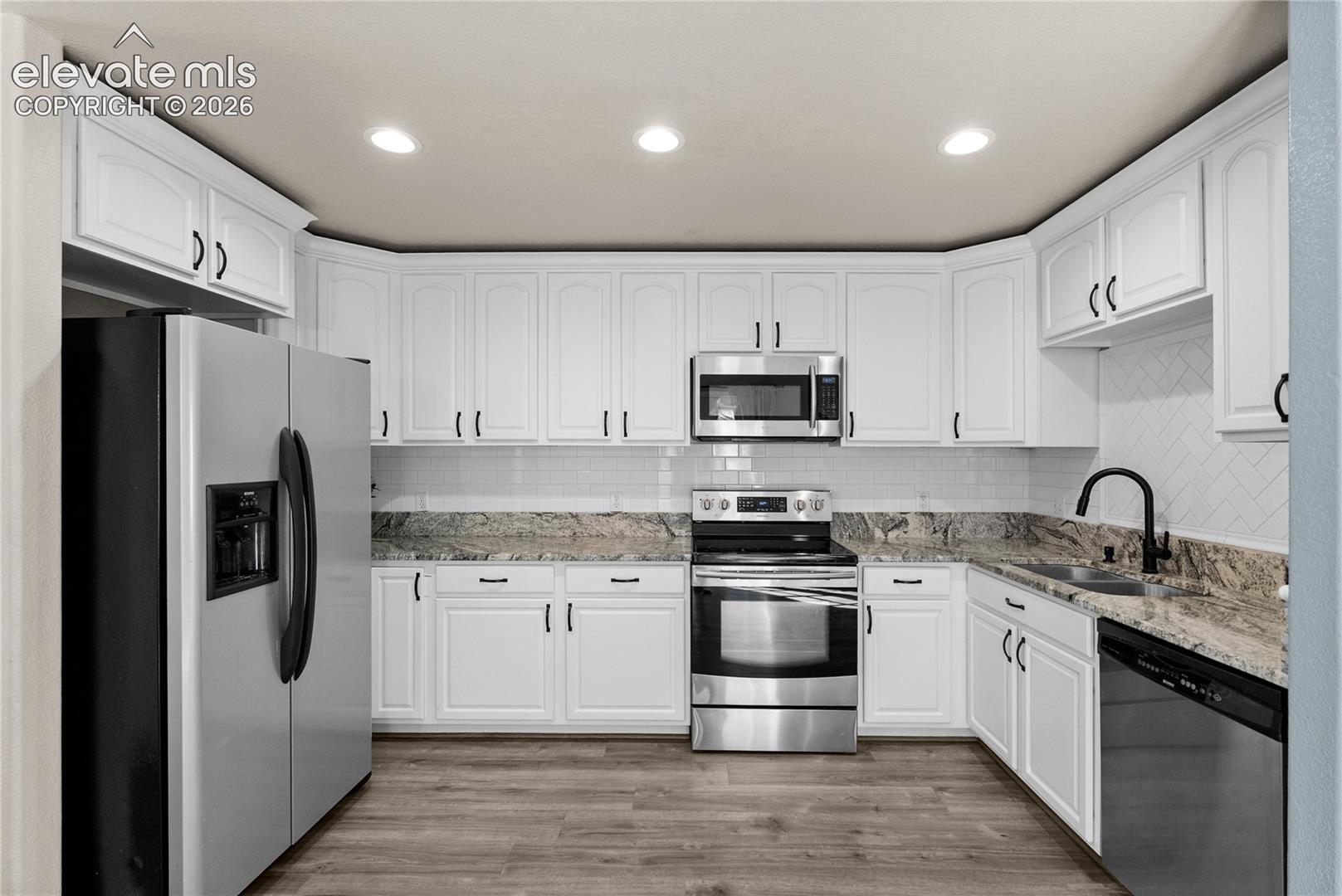 Bright kitchen featuring white cabinetry, stone countertops, stainless steel appliances, and wood-finish flooring