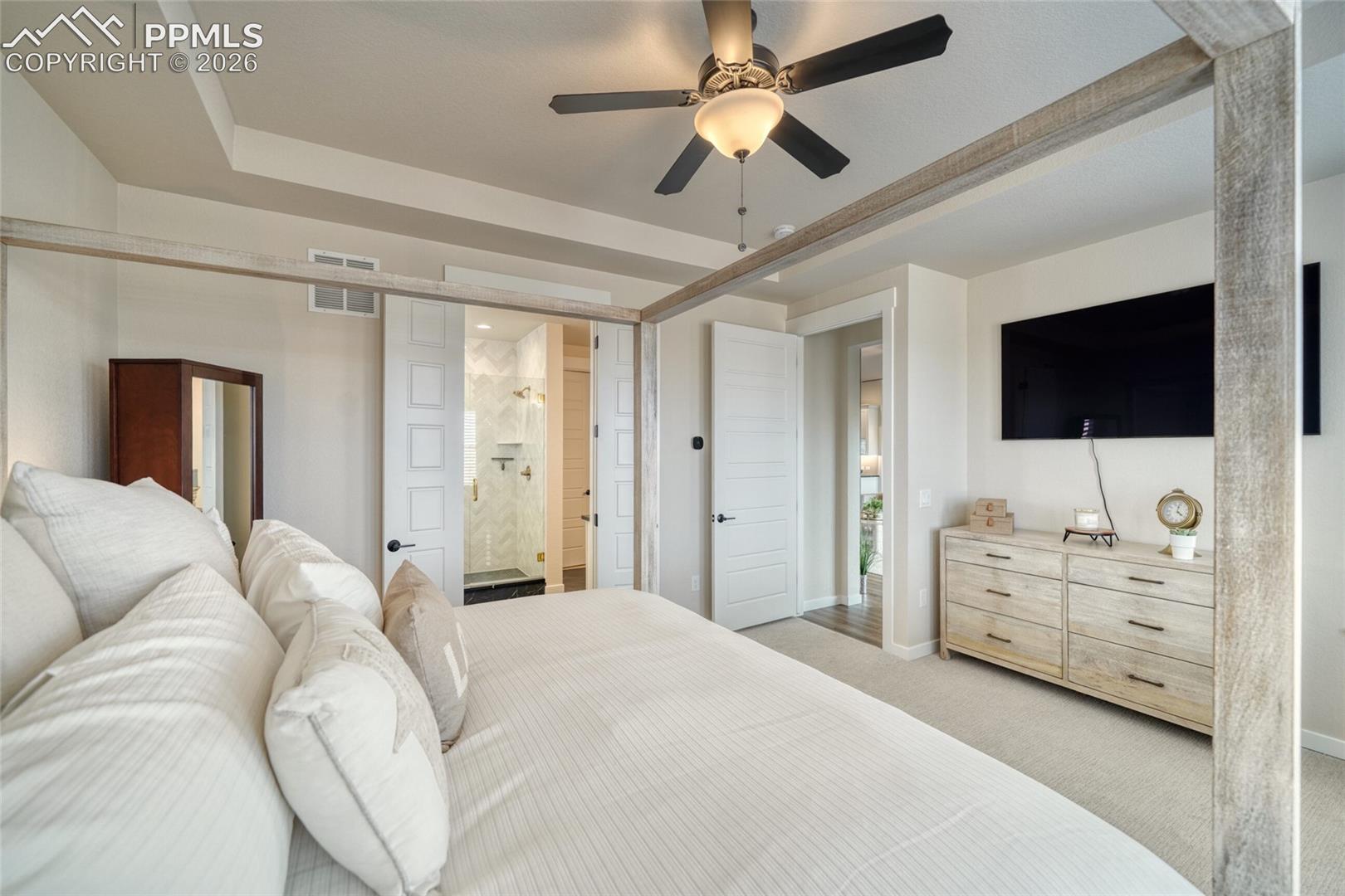 Bedroom featuring a tray ceiling, light carpet, a ceiling fan, and ensuite bathroom