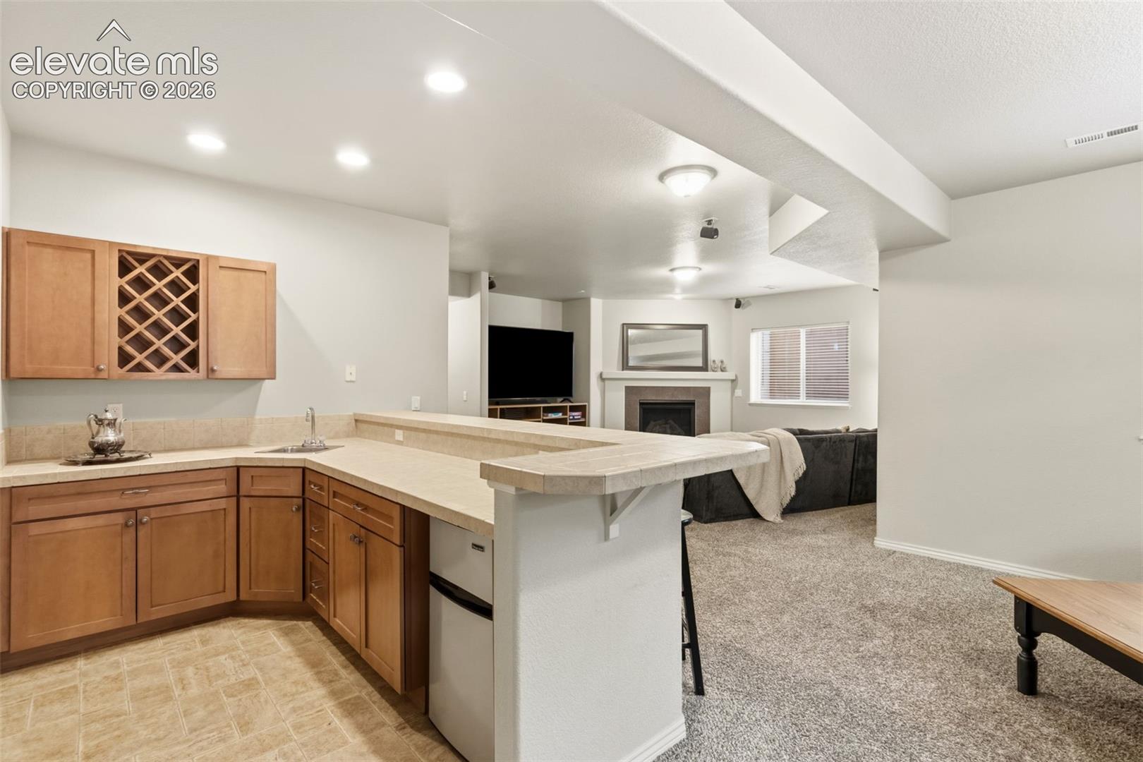 Kitchenette featuring wood cabinetry with a built-in wine rack, light-toned countertops, and a stainless steel sink with a chrome faucet