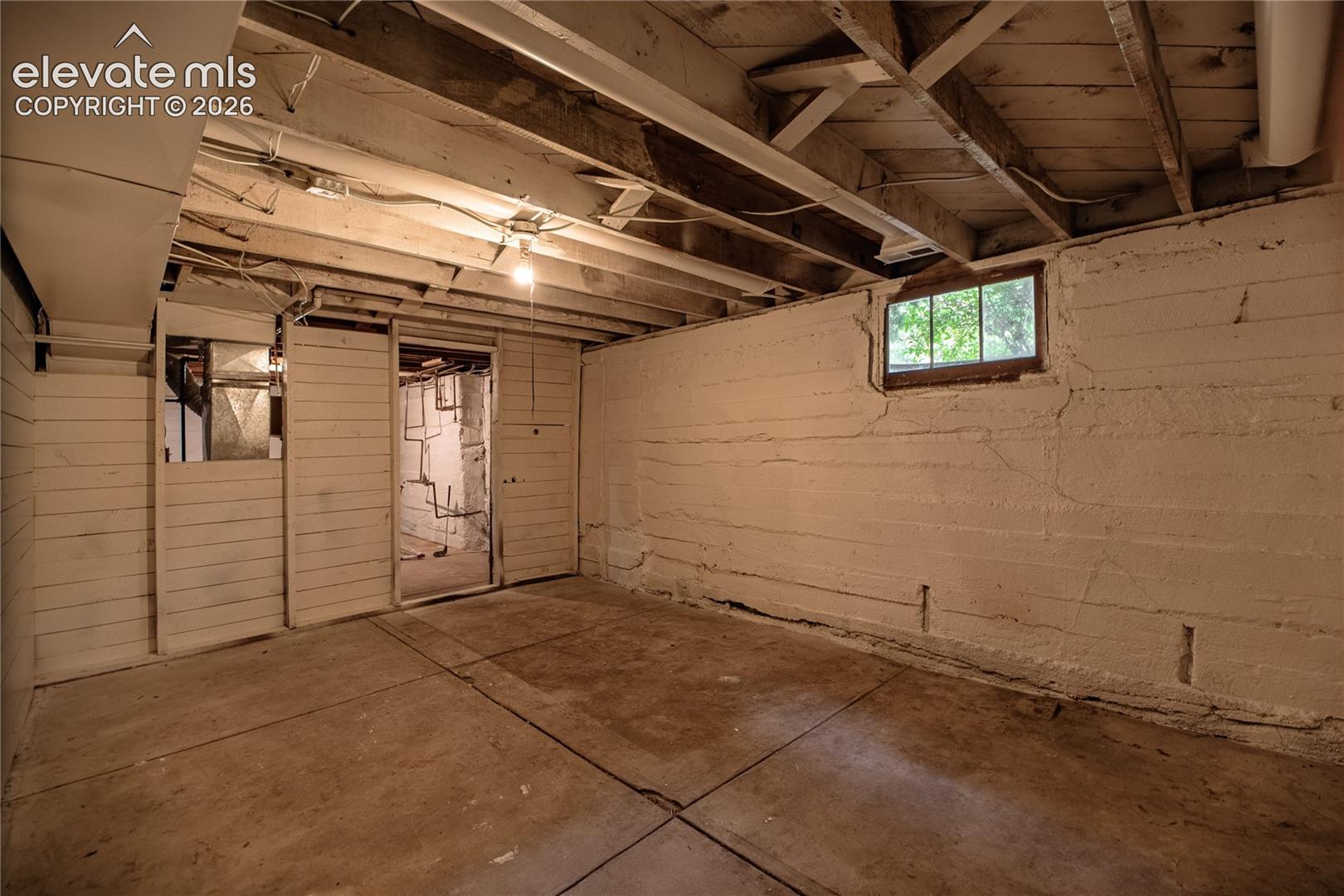 Unfinished basement space with exposed ceiling joists, concrete flooring, and a single-pane window
