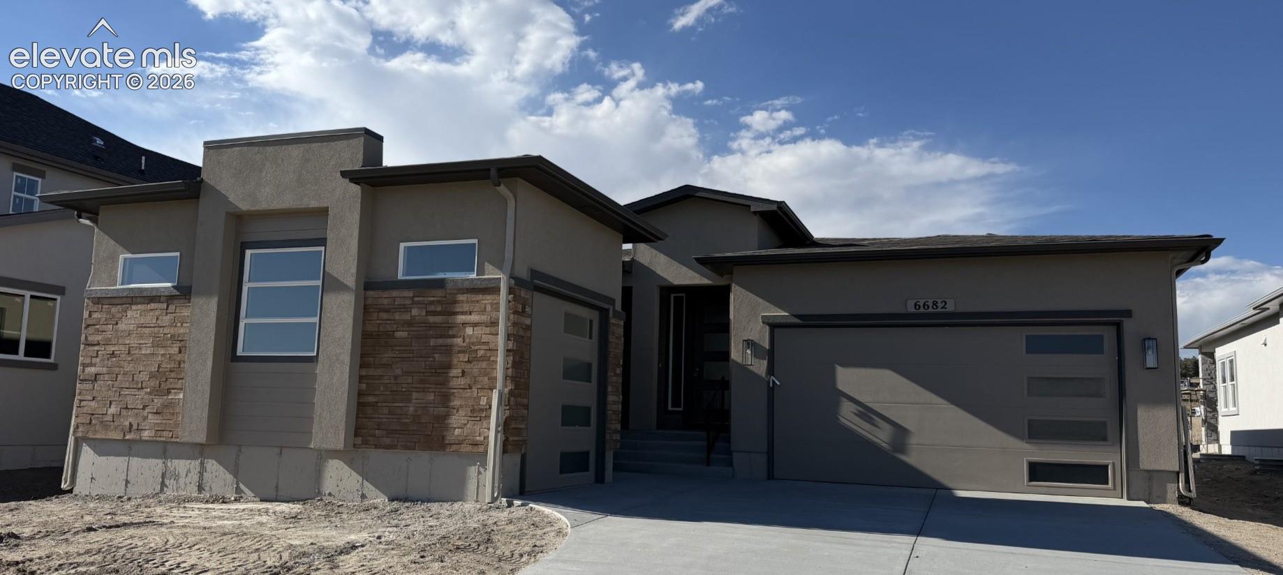 Contemporary exterior featuring stucco siding, stone veneer accents, multi-pane garage door with horizontal glass inserts, and concrete driveway