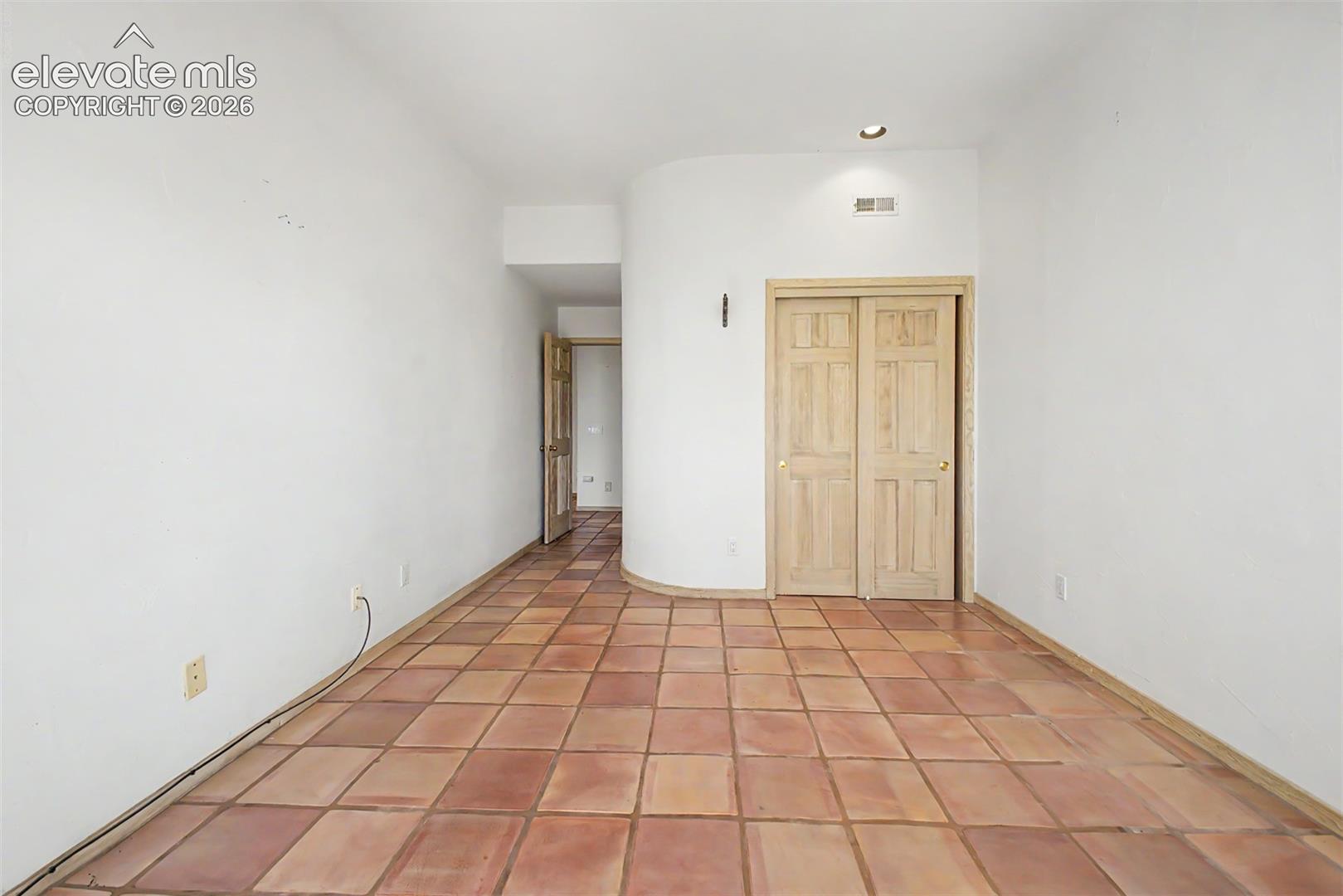 Terra cotta tile flooring, recessed lighting, and light wood-paneled bi-fold doors
