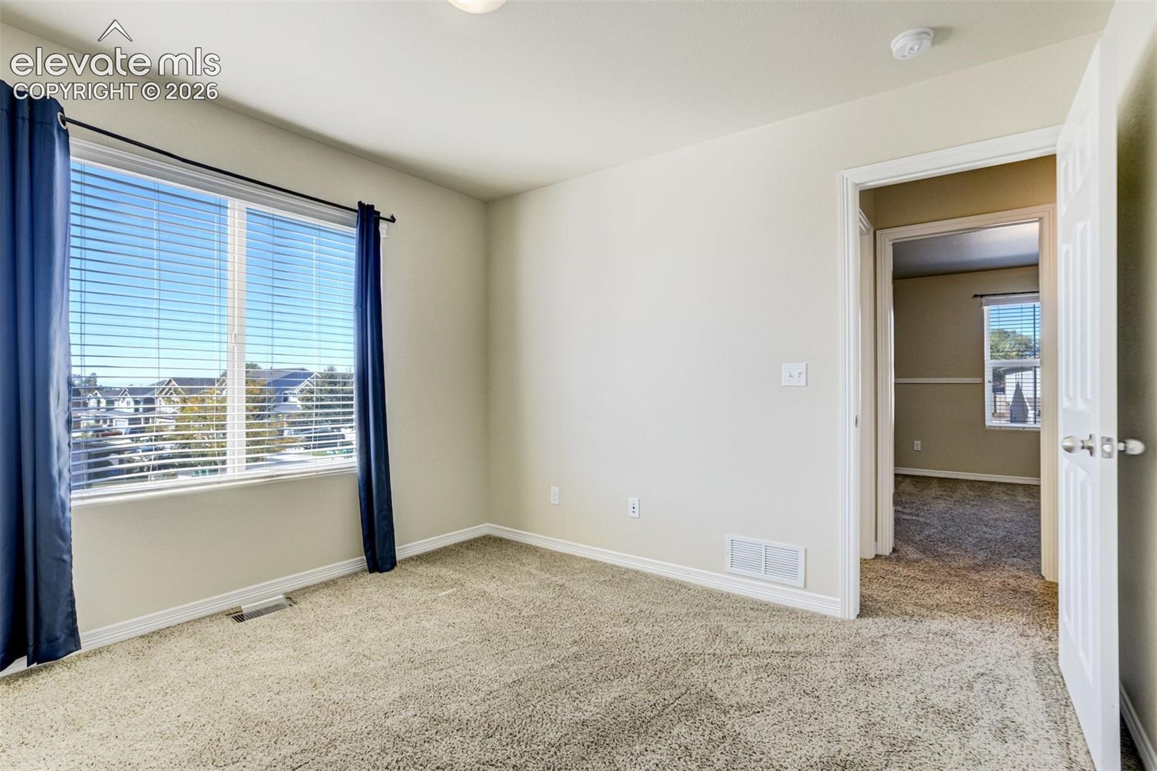 Carpeted flooring, white walls, large window with blinds, white trim, and a white interior door