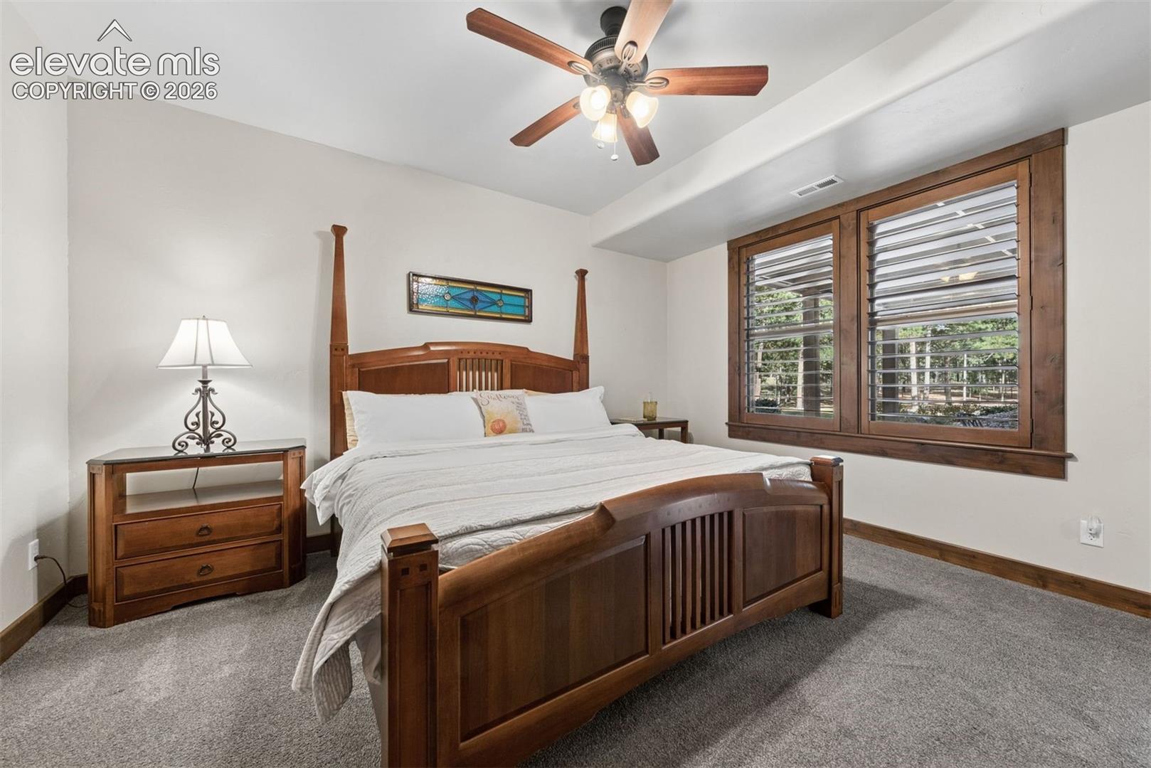 Room featuring neutral wall tones, plush wall-to-wall carpeting, wood-trimmed windows with integrated shutters, and a ceiling-mounted fan with light fixture