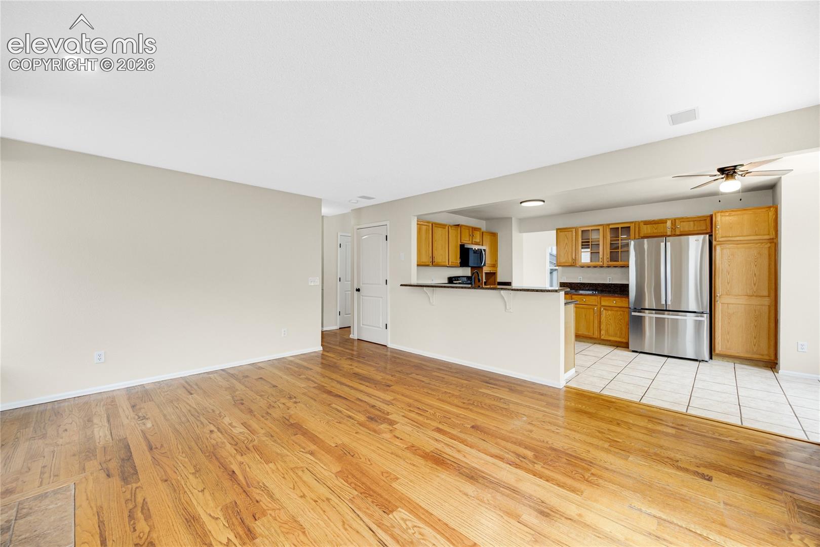 Open-concept area featuring wood-finish flooring, recessed lighting, a breakfast bar, stainless steel refrigerator, and tiled kitchen flooring
