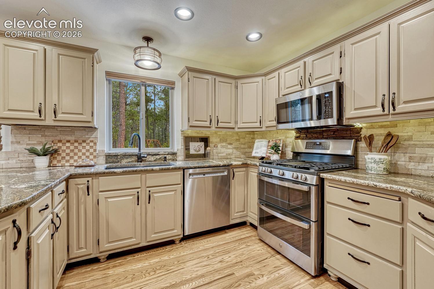 Kitchen featuring painted cabinetry, stone-finish countertops, stainless steel appliances, recessed ceiling lighting, and wood-finish flooring
