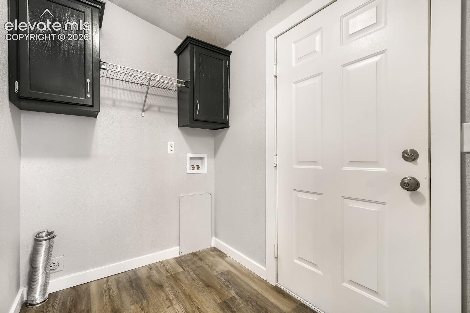 Utility area featuring wood-finish flooring, dark-finish upper cabinetry, wire shelving, and dedicated water and electrical hookups