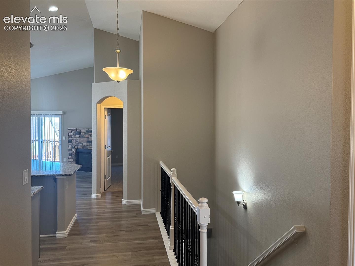 Vaulted ceilings, wood-finish flooring, wrought iron stair railing, arched entryway, and stone-accented fireplace
