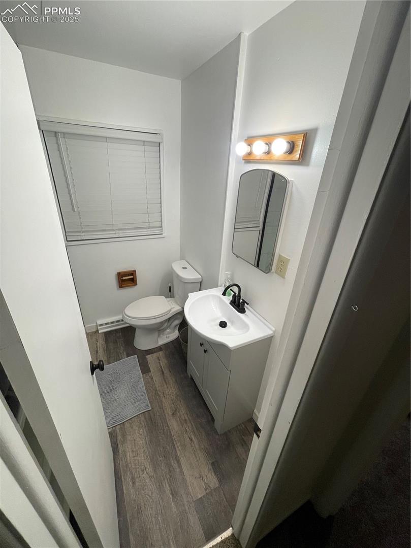 Half bath with wood finished floors, vanity, and baseboard heating