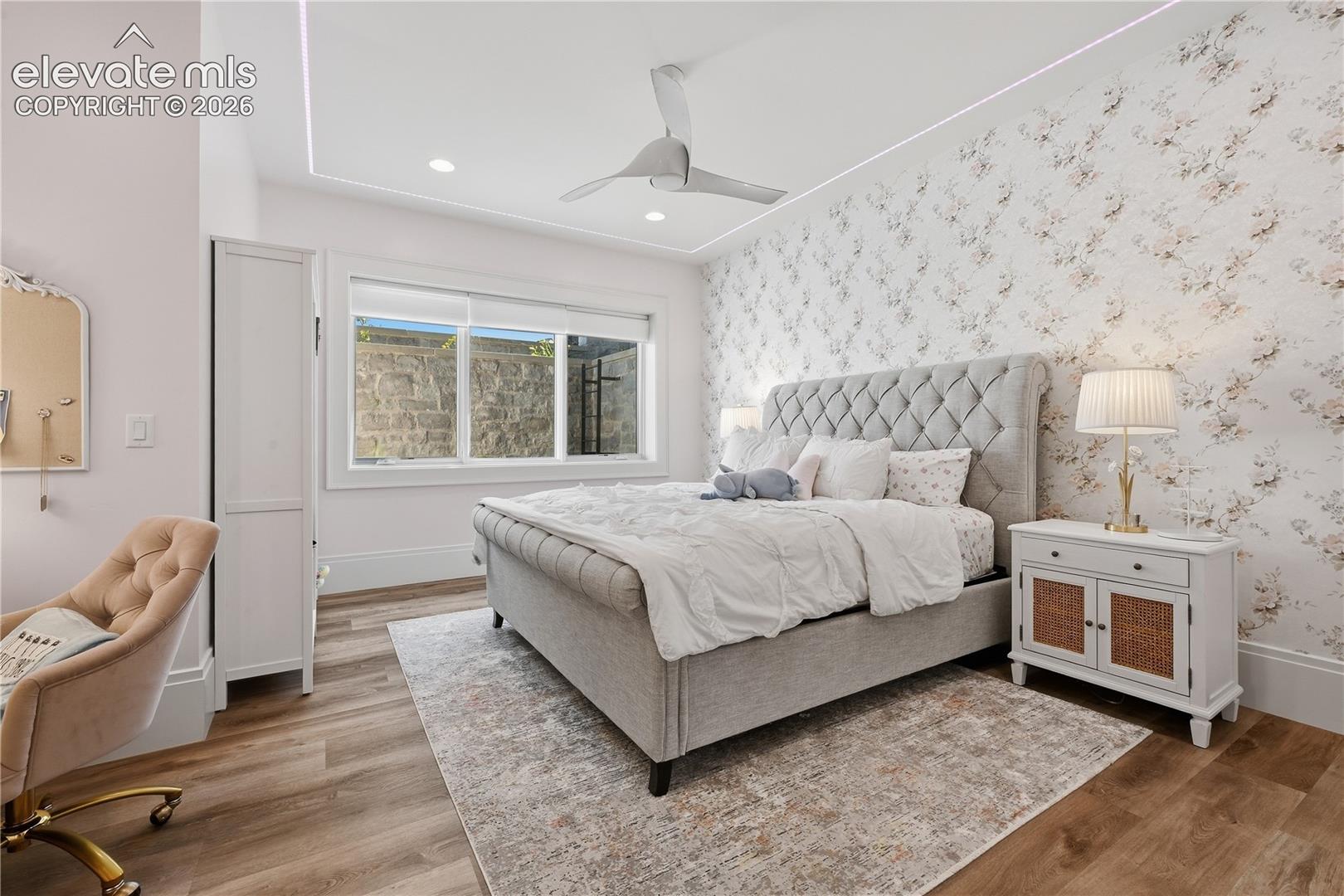 Wood-finish flooring, tray ceiling with recessed lighting, central ceiling fan, and decorative wall covering