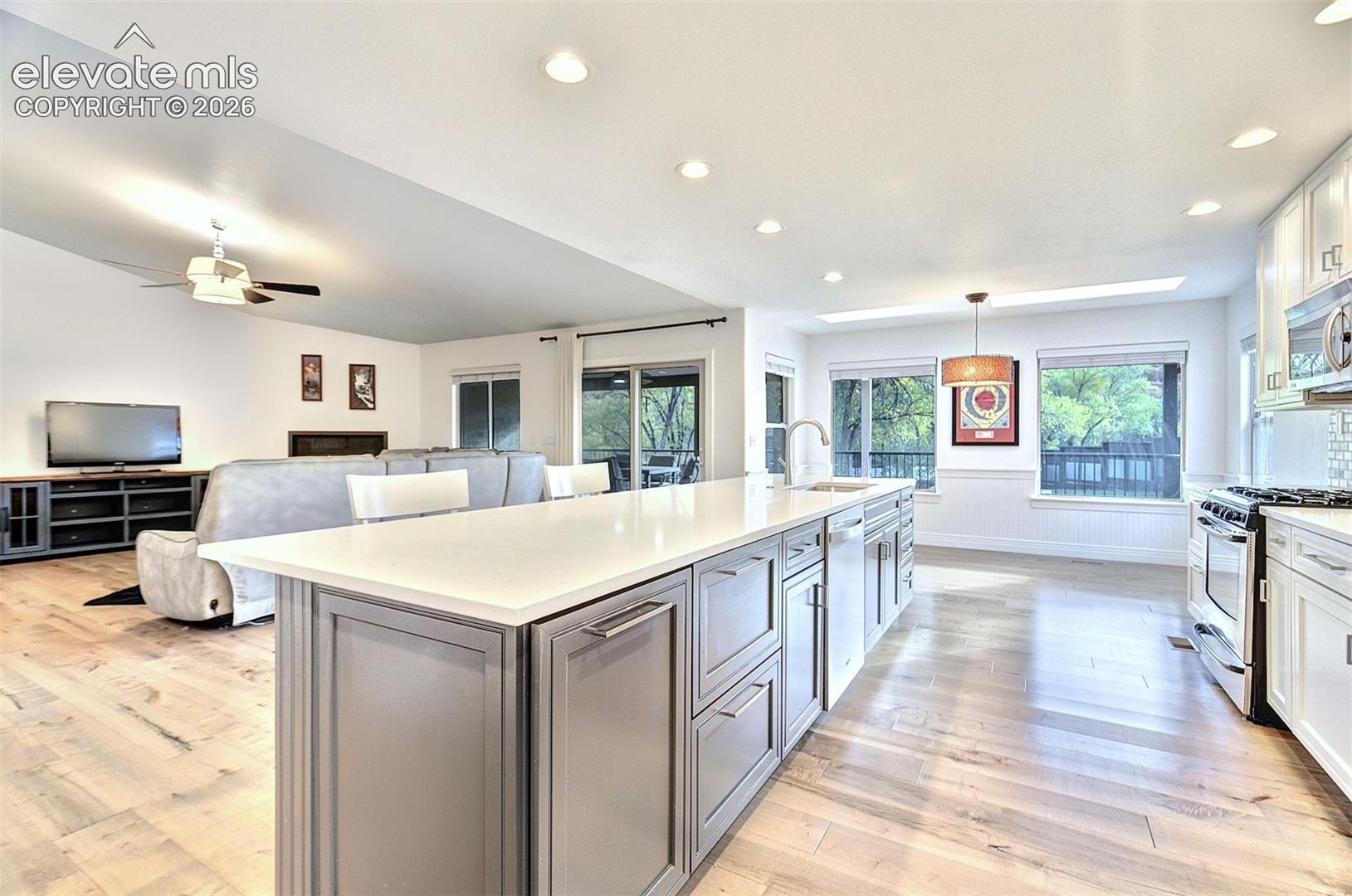Kitchen featuring an expansive island with a light-toned solid surface countertop, white shaker-style cabinetry, stainless steel appliances, and wood-finish flooring