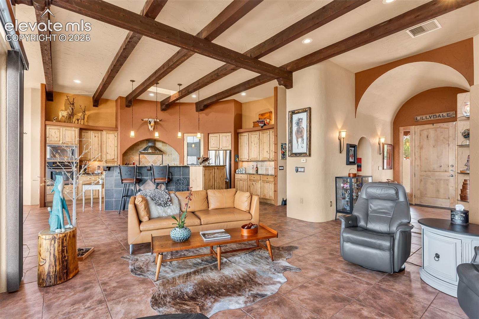 Open-concept interior featuring exposed wood ceiling beams, vaulted archways, ceramic tile flooring, built-in natural wood cabinetry, and recessed lighting