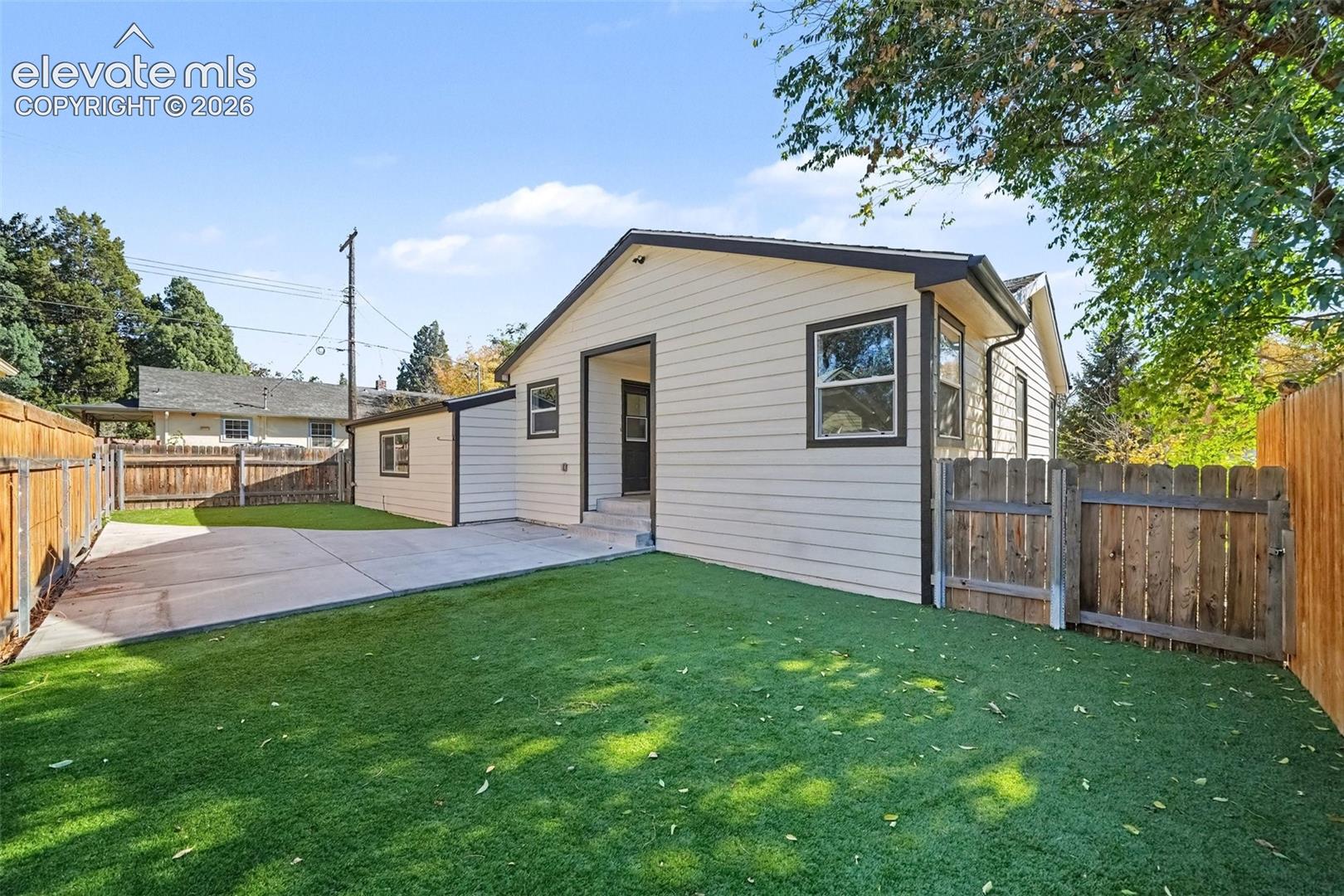Rear exterior featuring horizontal lap siding, a concrete patio, artificial turf, and wood perimeter fencing