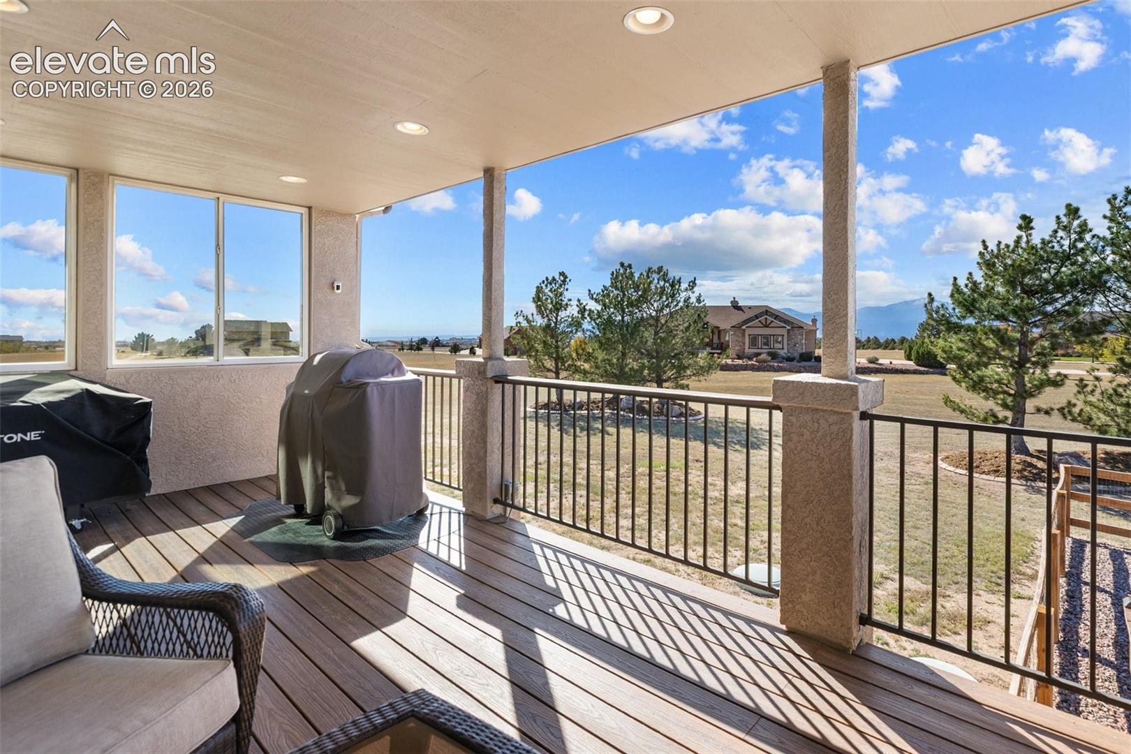 Covered outdoor deck featuring wood-finish decking, recessed lighting, and iron balustrades set against a backdrop of mountainous terrain