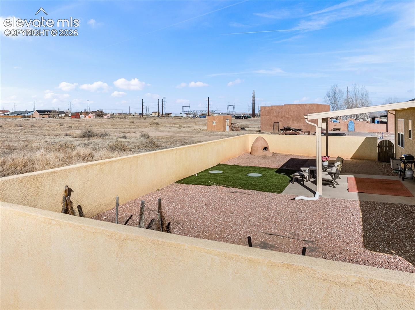 Walled backyard featuring a covered patio, gravel landscaping, and a built-in outdoor oven