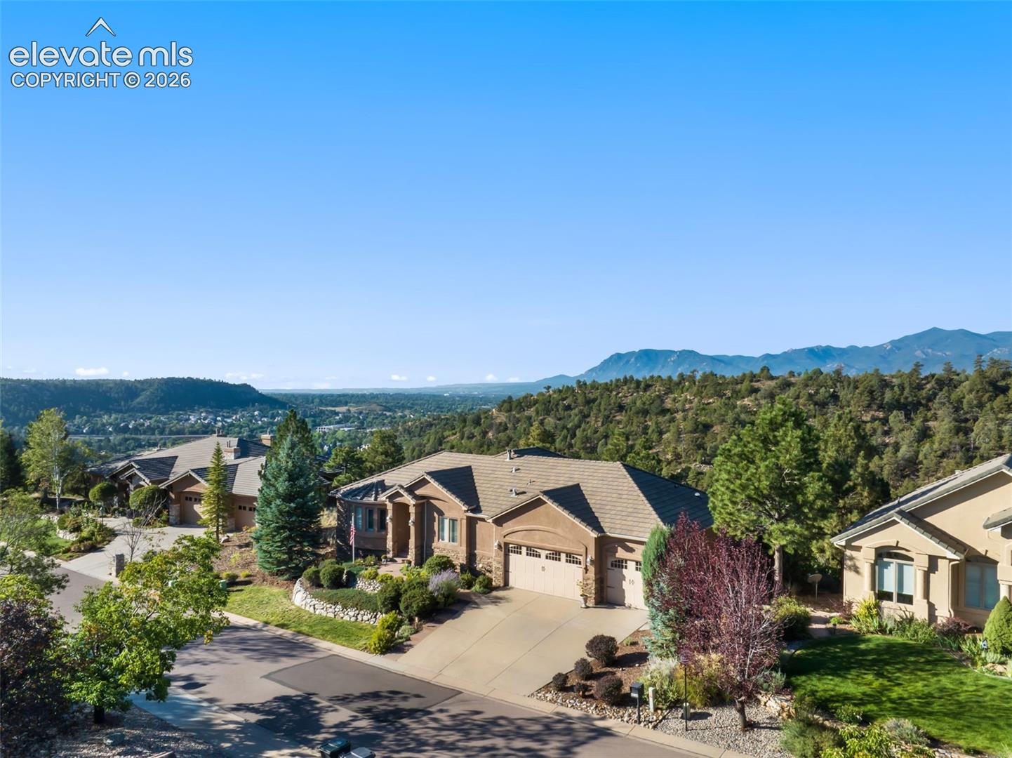 Single-story residence featuring a multi-gabled exterior, concrete driveway, attached multi-car garage, stone retaining wall, and mountain backdrop. views to Cheyenne Mountain and beyond