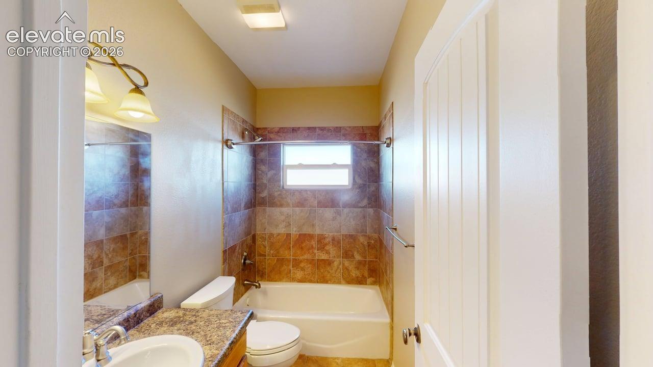 Bathroom featuring a single vanity with an integral sink, a tiled tub/shower combination, and a window for natural light