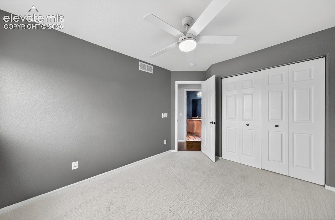 Neutral-toned room featuring gray walls, light-colored carpeting, a ceiling-mounted light fixture with a fan, and a double-panel closet with white doors
