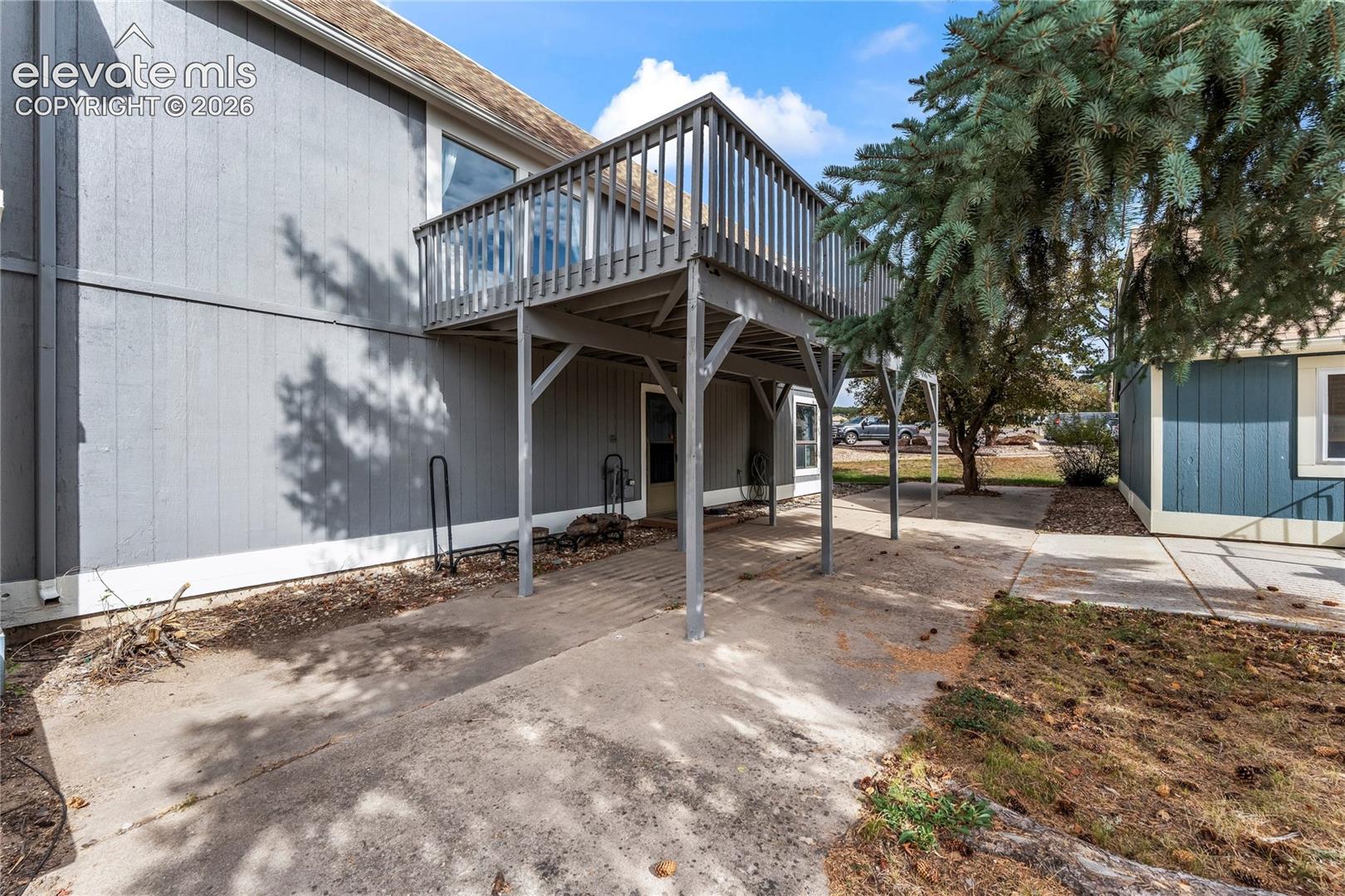 Elevated wooden deck with vertical rail balusters, concrete patio, and vertical panel exterior siding