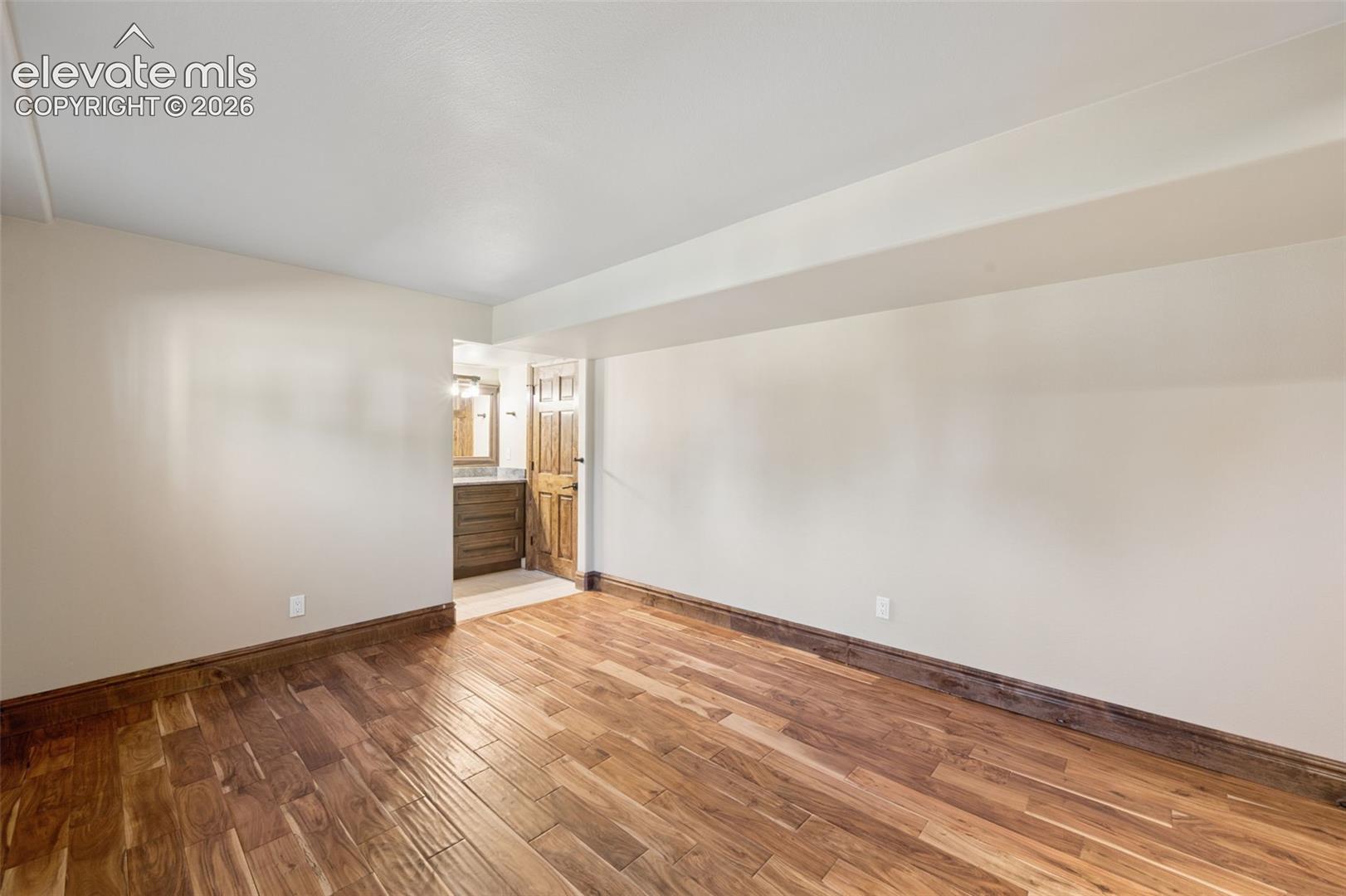 Basement bedroom. Interior space featuring wood-finish flooring, dark wood-tone trim, and neutral wall coloring
