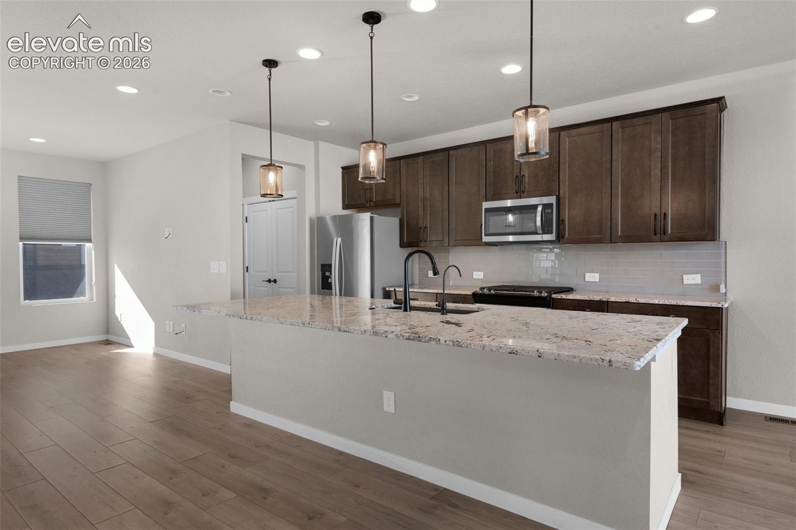 Kitchen featuring a large island with a stone countertop, dark wood-finish cabinetry, stainless steel appliances, and pendant lighting