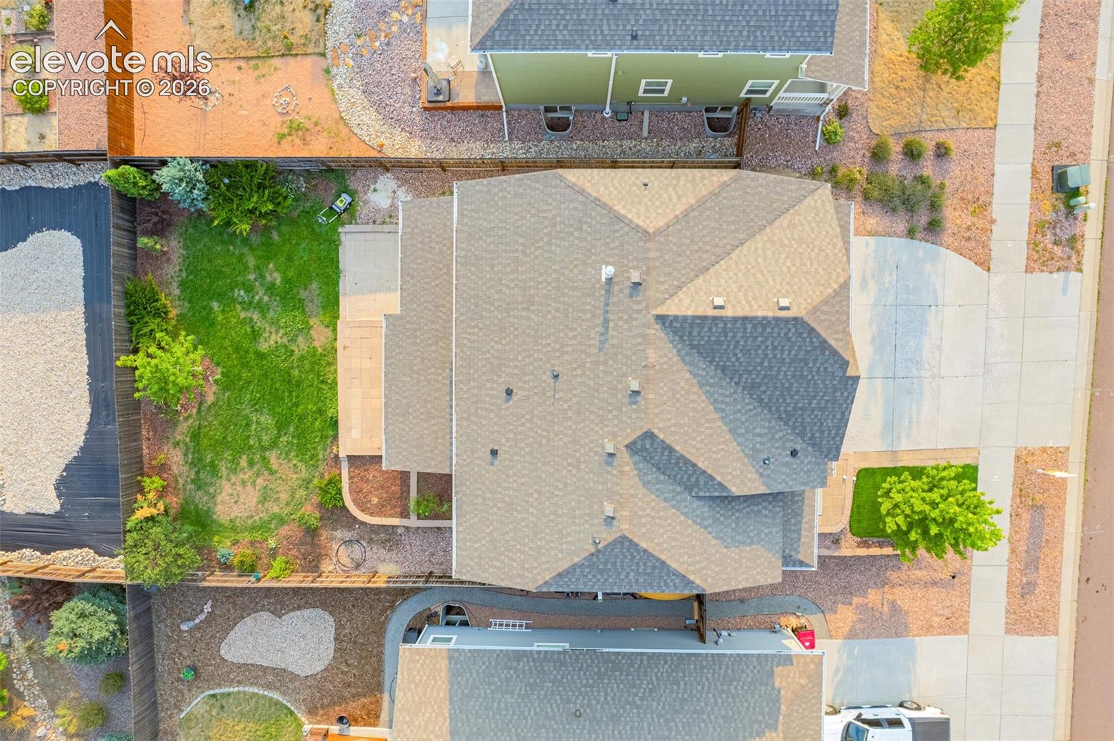 Asphalt shingle roof, concrete driveway, concrete patio, grass lawn, and mature landscaping