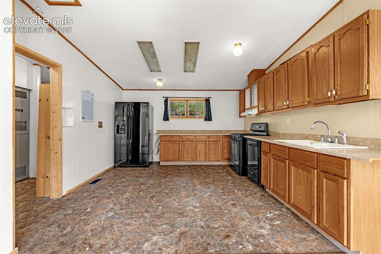Kitchen featuring wood-finish cabinetry, black appliances, a double basin sink, and a light-colored countertop