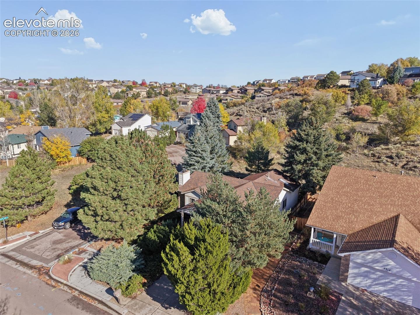 Aerial perspective featuring established landscaping, mature evergreen trees, and hillside topography