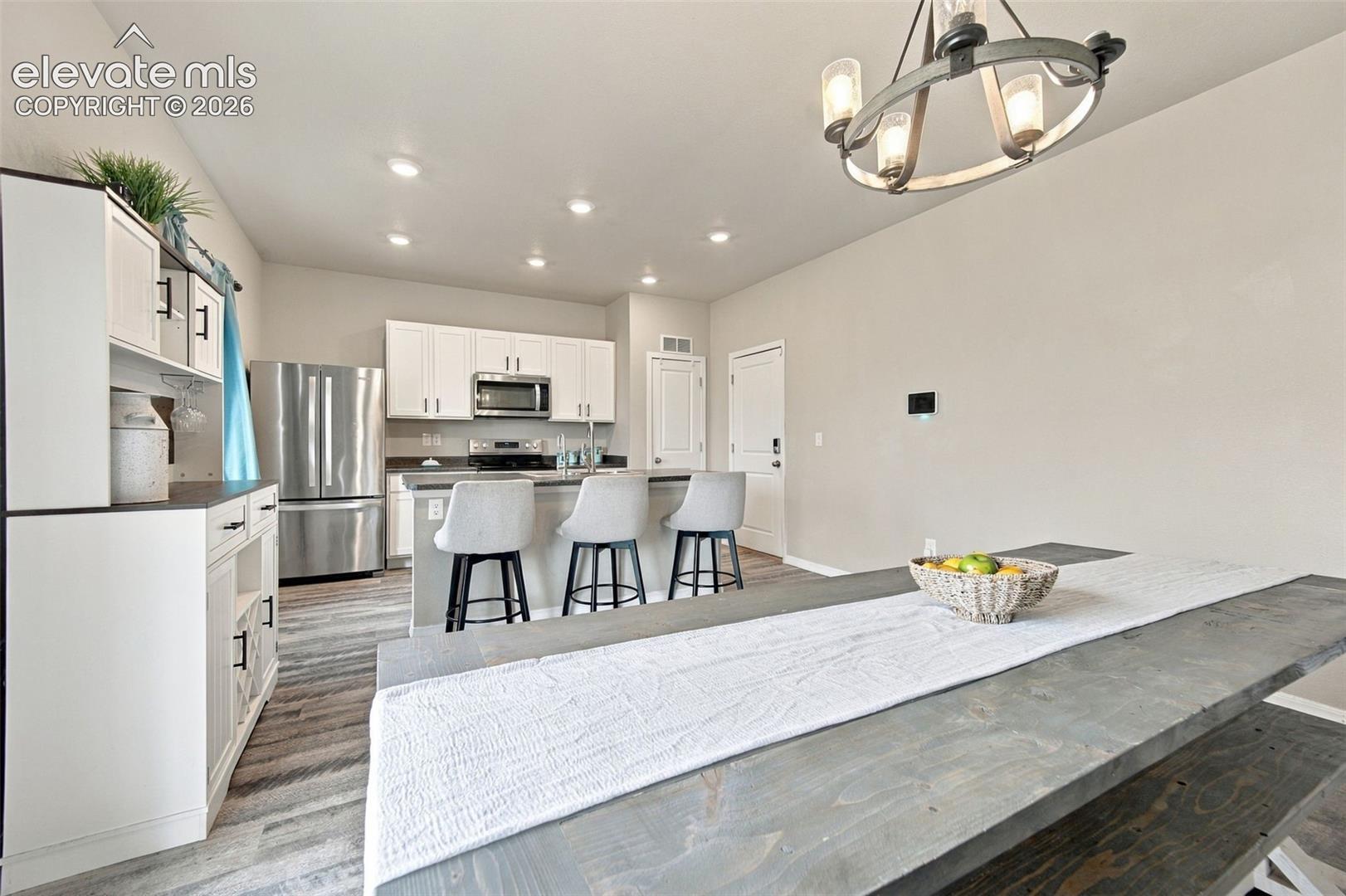 Kitchen featuring white shaker-style cabinetry, stainless steel appliances, a kitchen island with seating, recessed lighting, and wood-finish flooring