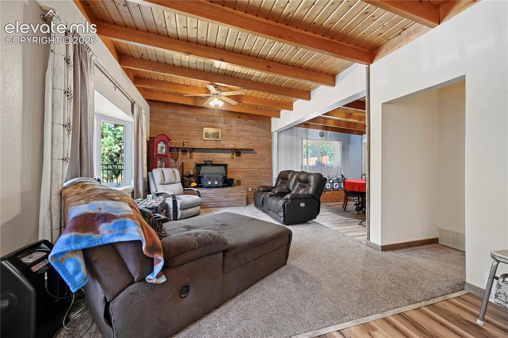 Wood-paneled vaulted ceiling with exposed beams, brick-clad fireplace, and ceiling fan