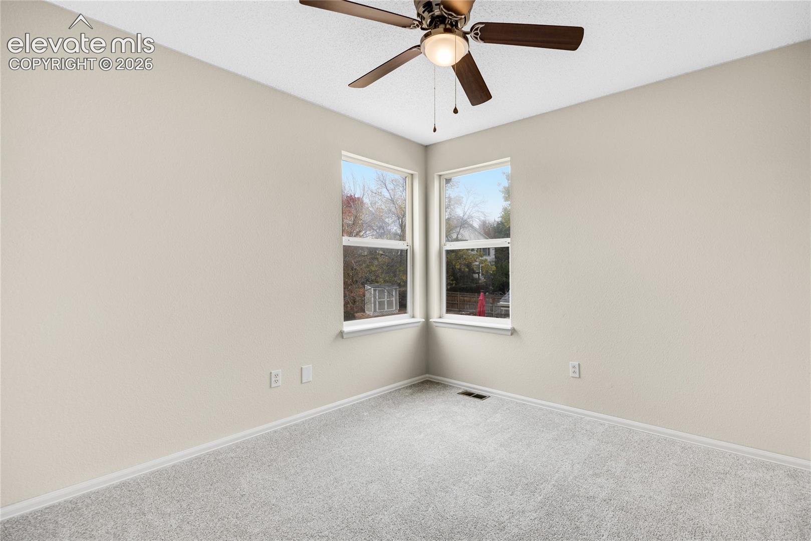 Neutral-toned interior featuring wall-to-wall carpeting, dual windows, and a ceiling-mounted light fixture with fan