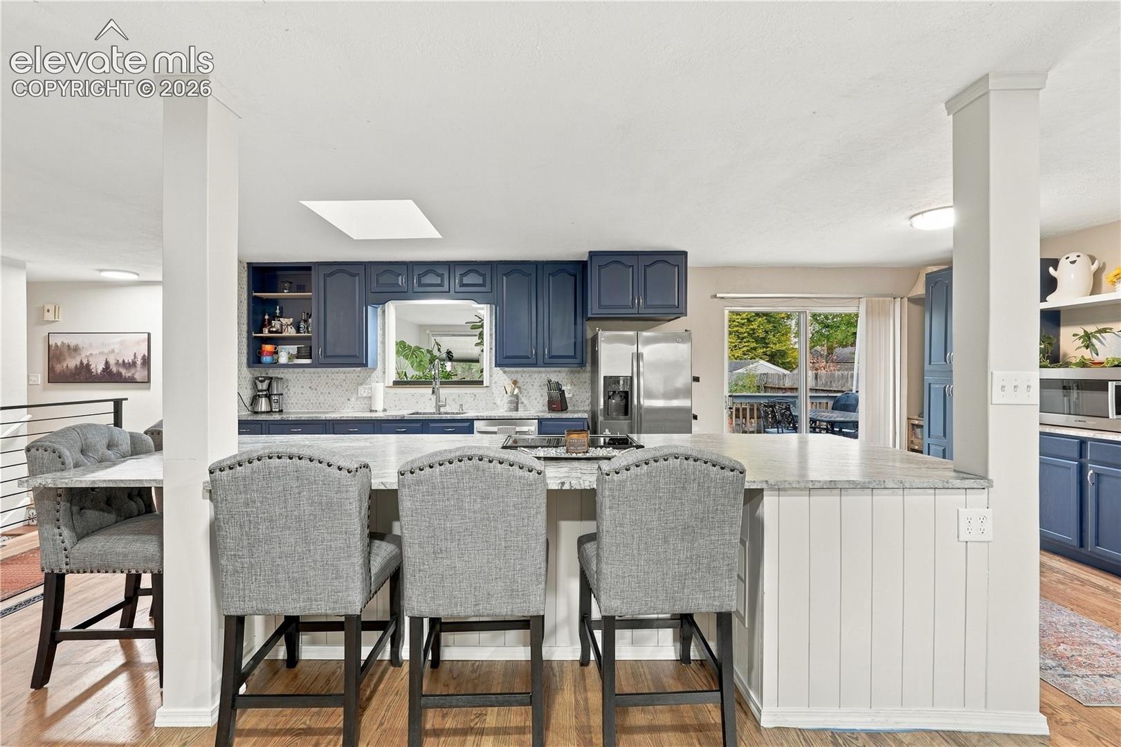 Kitchen featuring navy blue cabinetry, a large stone-surface island, stainless steel refrigerator, beadboard island paneling, and recessed lighting
