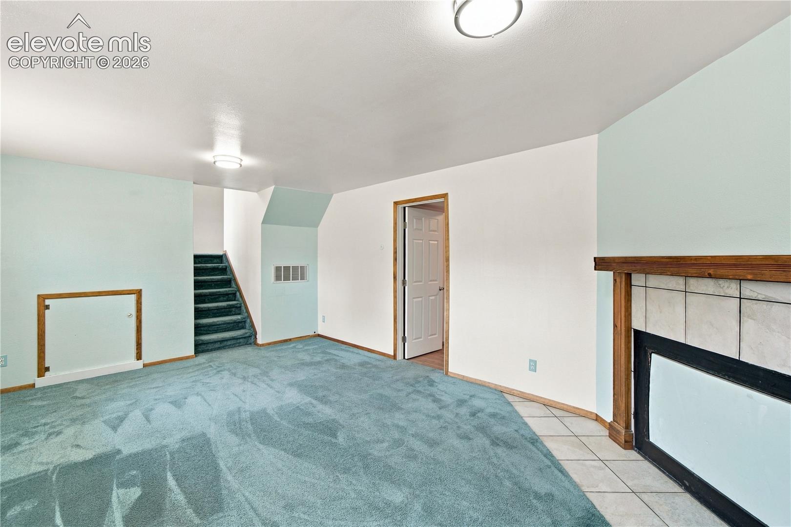 Tile-surround fireplace with a wood mantle, recessed door with wood trim, and a staircase with wall-to-wall carpeting