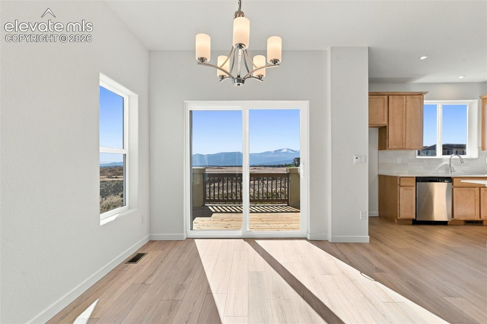 Open concept living area featuring light wood-finish flooring, a contemporary chandelier, and a sliding glass door opening to an outdoor deck