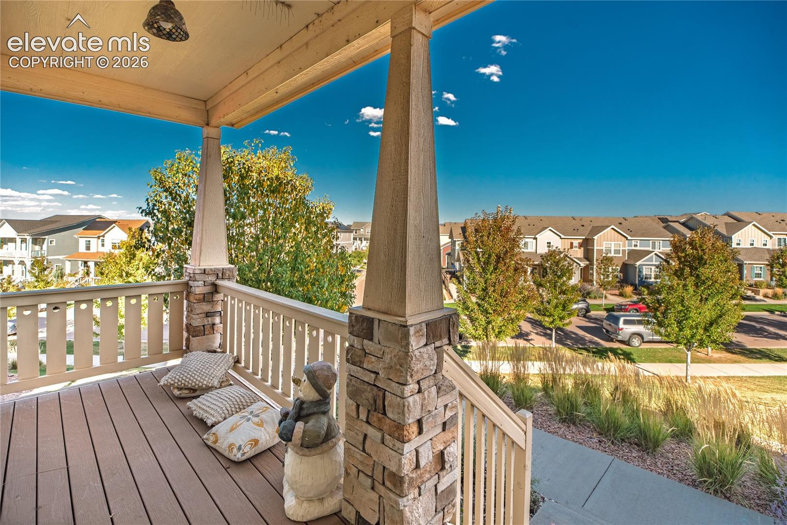 Covered porch featuring composite decking, stacked stone pillar bases, and painted railings
