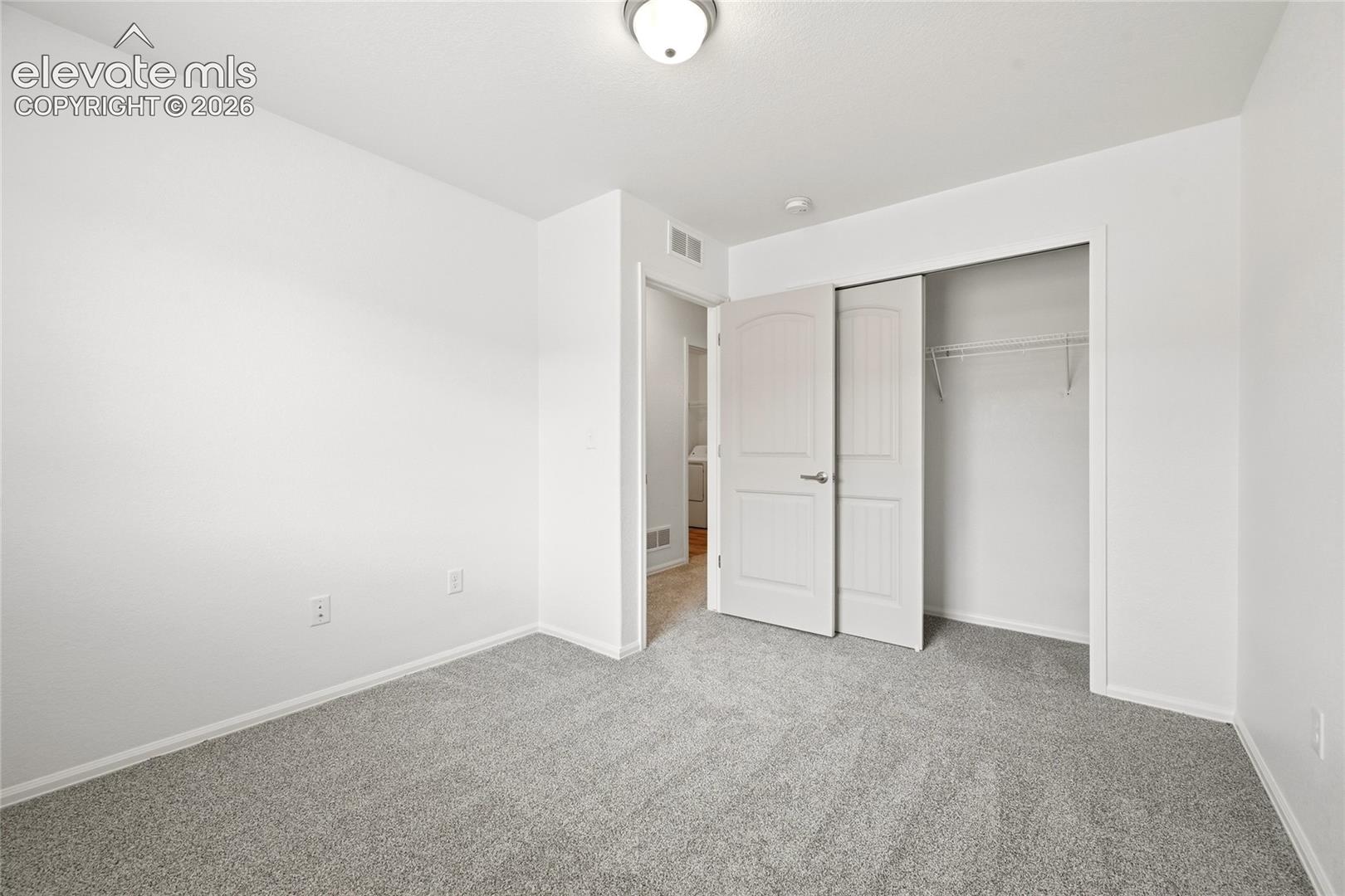 Neutral-toned carpeting, two-panel interior doors, flush-mount ceiling lighting, and built-in closet shelving