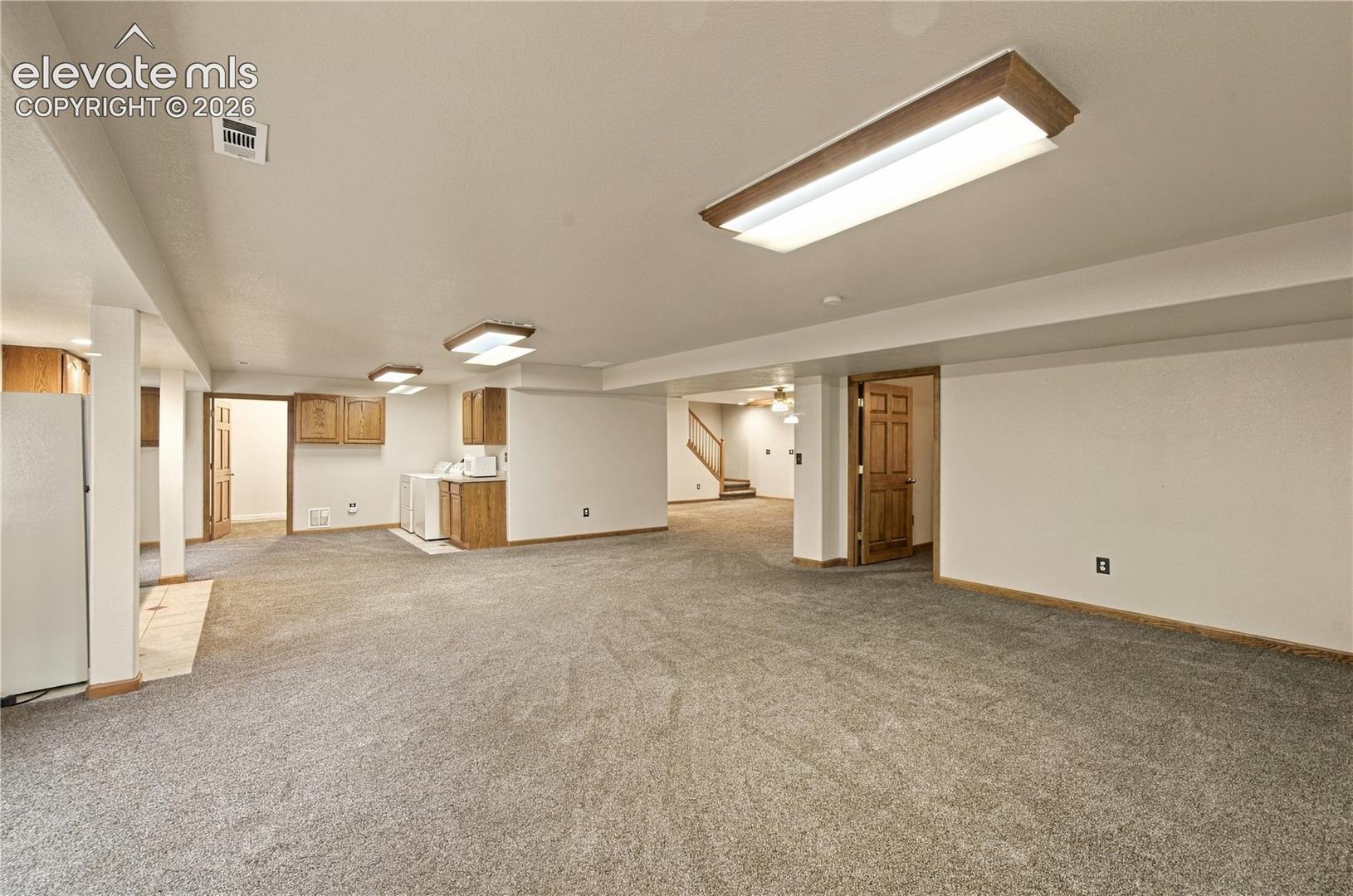 Open interior space featuring wall-to-wall carpeting, wood-finish cabinetry, rectangular flush-mount lighting fixtures, and solid wood interior doors
