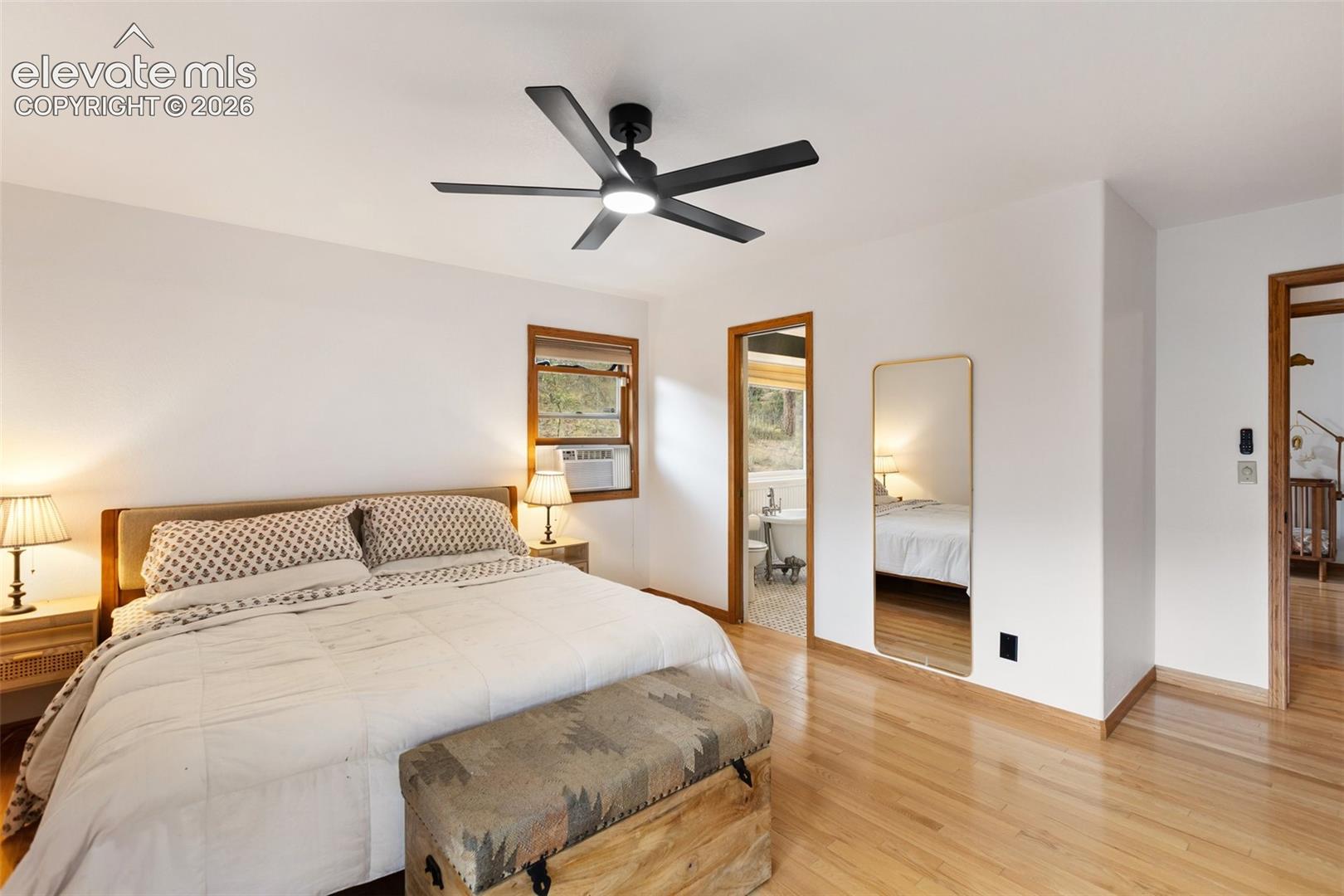 Room with hardwood flooring, matte black multi-blade ceiling fan with integrated lighting, and wooden door trim