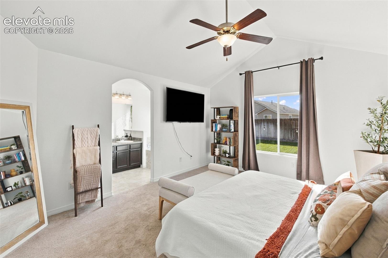 Vaulted ceilings, neutral carpeting, ceiling fan with light fixture, and arched entryway