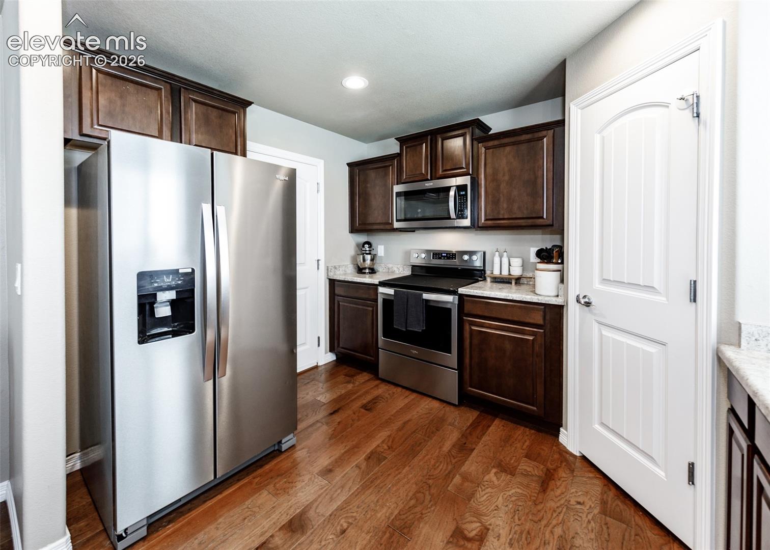 Kitchen featuring dark wood cabinetry, stainless steel appliances, wood-finish flooring, and solid-surface countertops