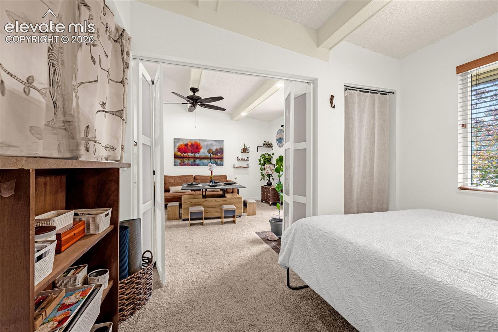 Vaulted ceiling with exposed beams, ceiling fan, carpeted flooring, and privacy blinds