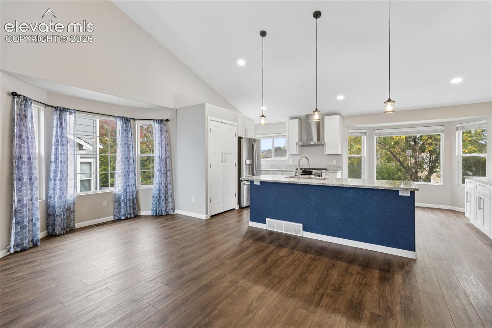 Vaulted ceilings, wood-finish flooring, kitchen island with stone countertop, stainless steel appliances, and bay windows